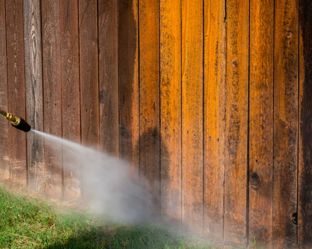 Man pressure washing a dirty fence to remove dirt, grime, and pollen buildup.