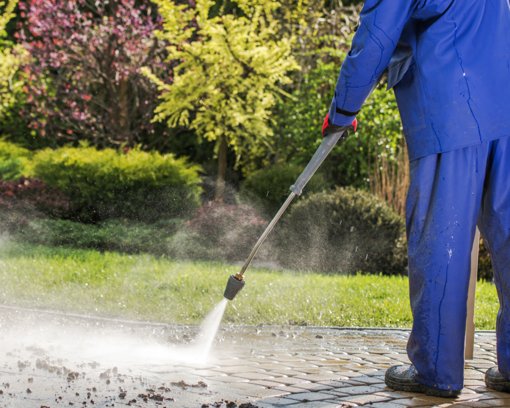 Man using a pressure washer to clean a dirty sidewalk covered in grime and buildup.