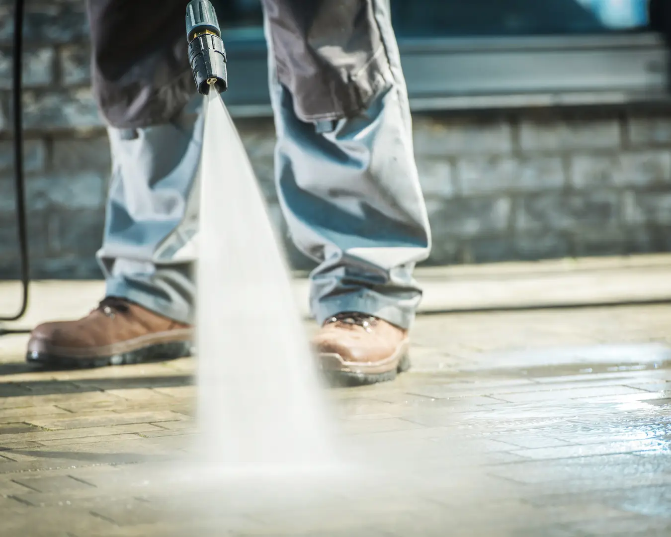 Close up of man wearing boots and jeans pressure washing outdoor walkway.