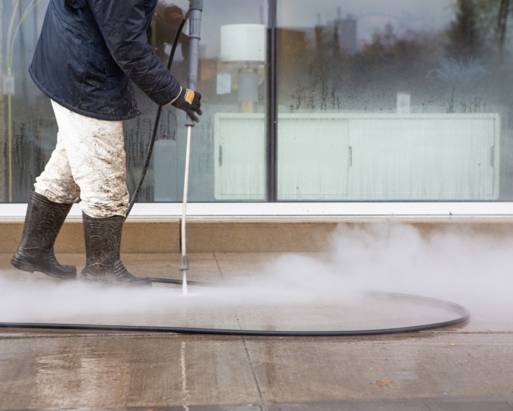 Close up of man pressure washing sidewalk of commercial building.