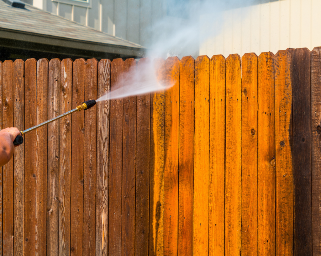Male hand holding power washer, cleaning dirty, wooden fence.
