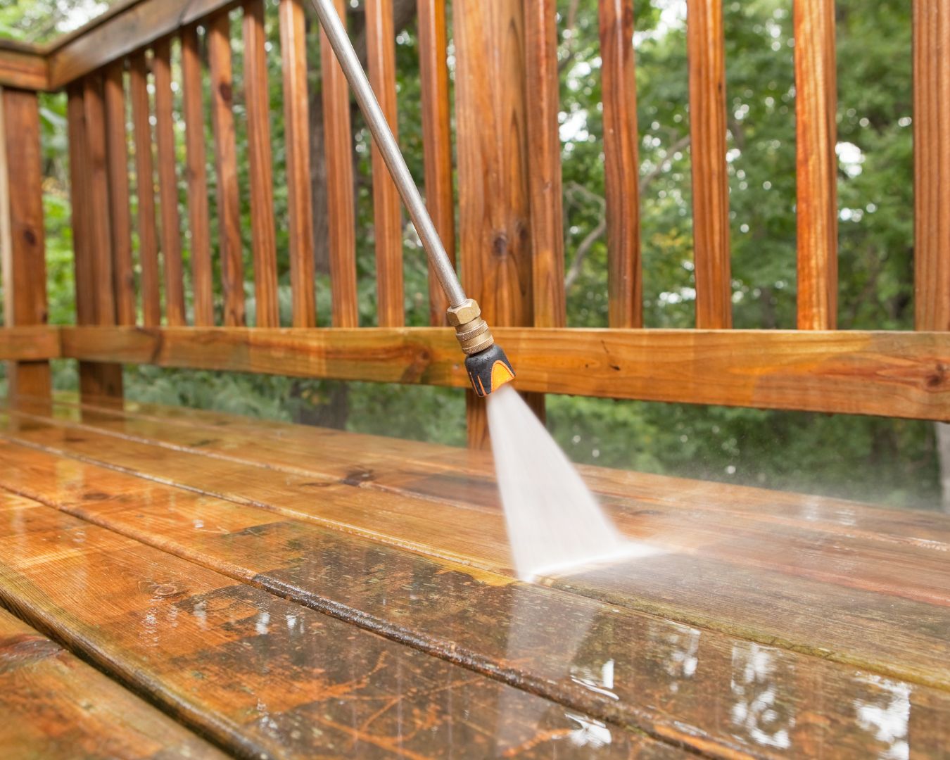 Close up pressure washer removing stains from wooden deck.