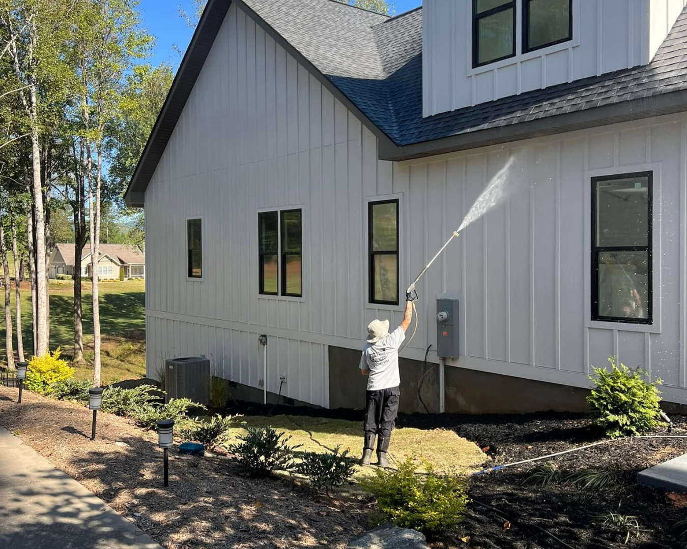 Team member of Shane's Power House Washing, pressure washing the side of beautiful, modern residential home.