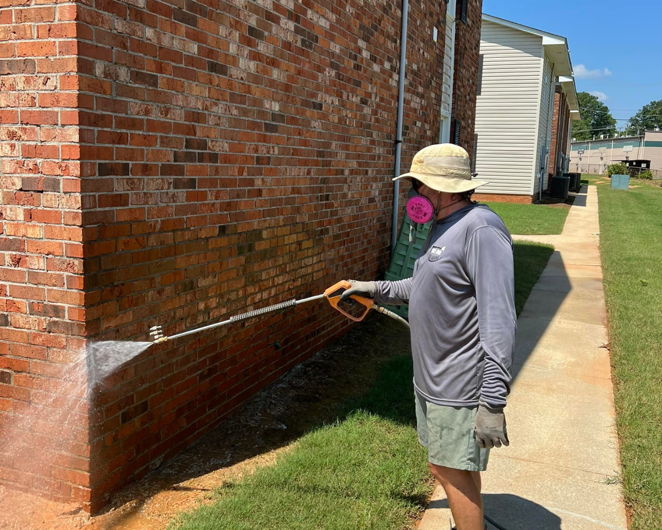 Shane's Power House Washing team member pressure washing brick wall of outside of building, wearing mask.