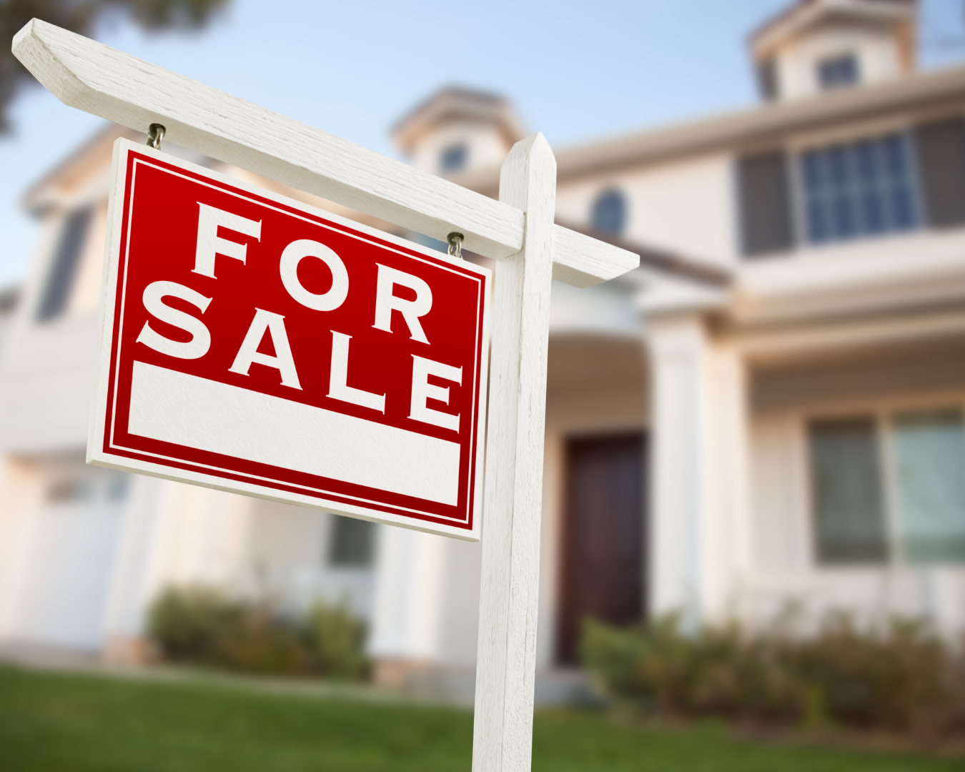 Blurred image of large residential home, with shot focused on "For Sale" sign.