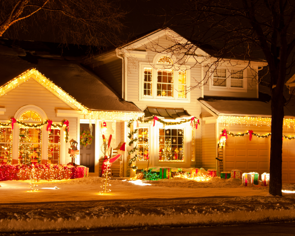 A suburban home at night decorated with bright Christmas lights, garlands, and ornaments, glowing warmly against a snowy winter landscape.