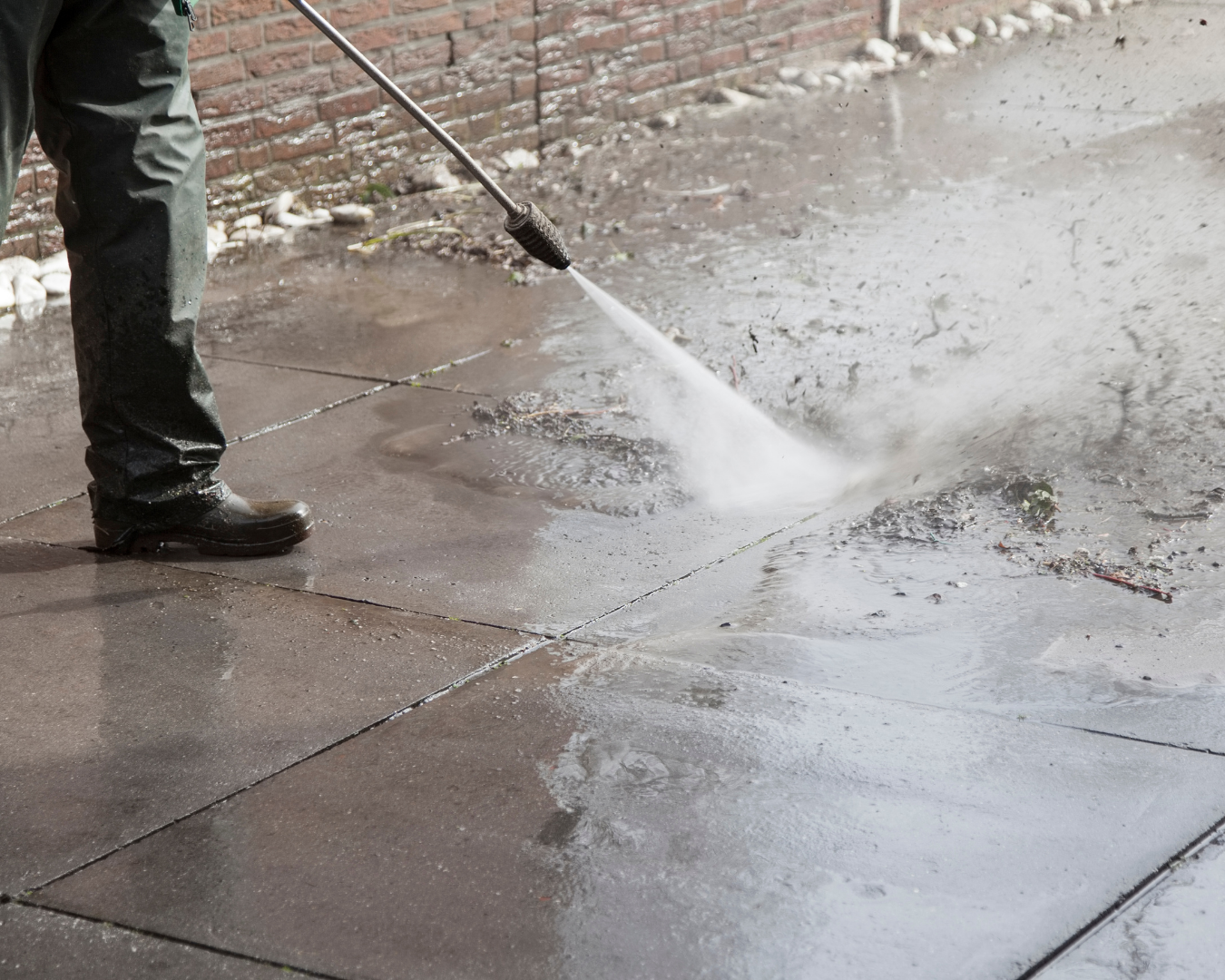 Professional pressure washing a concrete walkway to remove algae, moss, and grime during wet winter conditions.