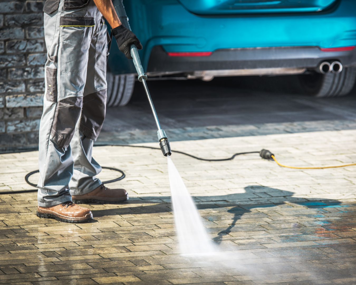 Man using a pressure washer to clean a driveway, removing dirt and grime.