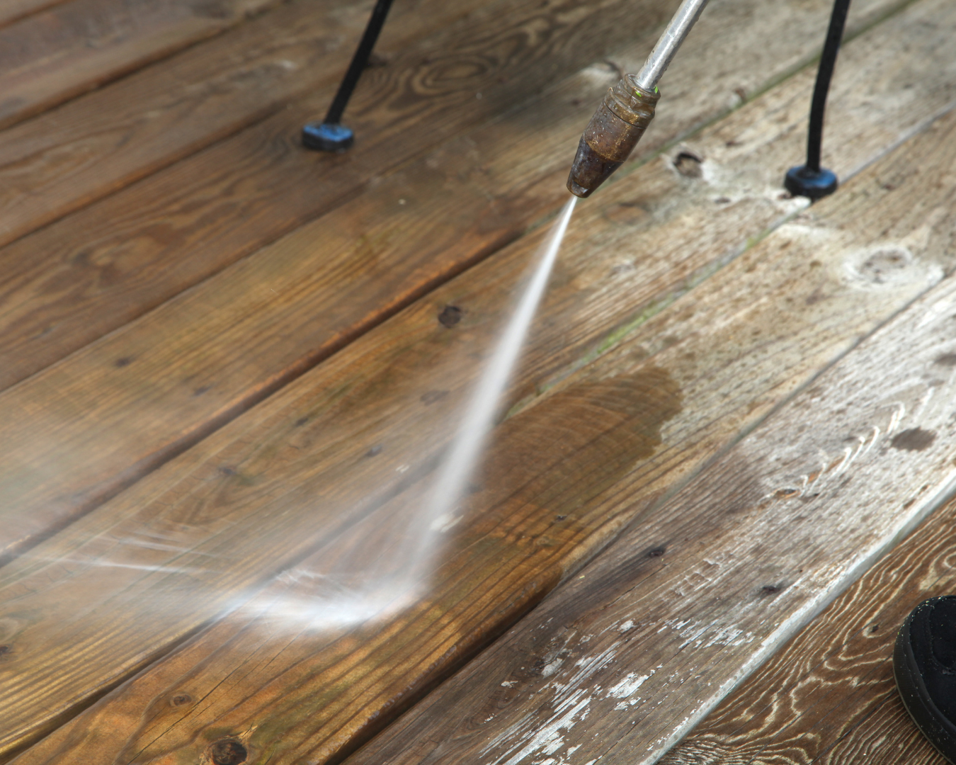 This close-up action shot shows a high-pressure water stream stripping away years of grime, algae, and weathered gray oxidation from a wooden deck, revealing the rich, natural brown grain underneath.