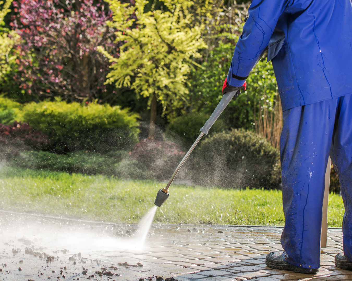 Man using a pressure washer to clean a dirty sidewalk covered in grime and buildup.