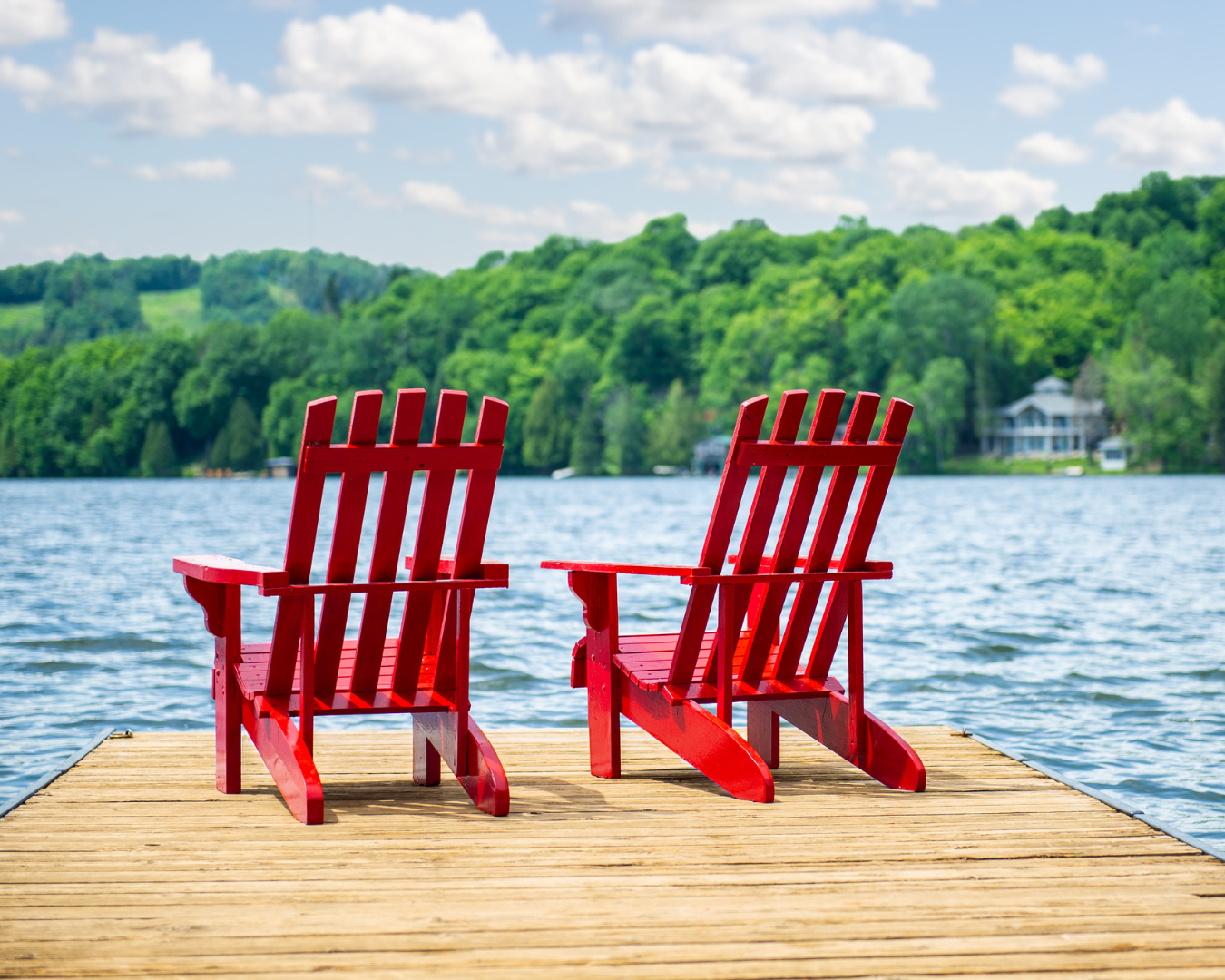 This tranquil scene captures two iconic red Adirondack chairs (also known as Muskoka chairs) resting on a wooden dock, overlooking a calm lake and lush, forested hills. While this looks like the ultimate spot for a morning coffee, homeowners in Anderson, SC, know that a dock like this can become a major slip hazard in the spring.