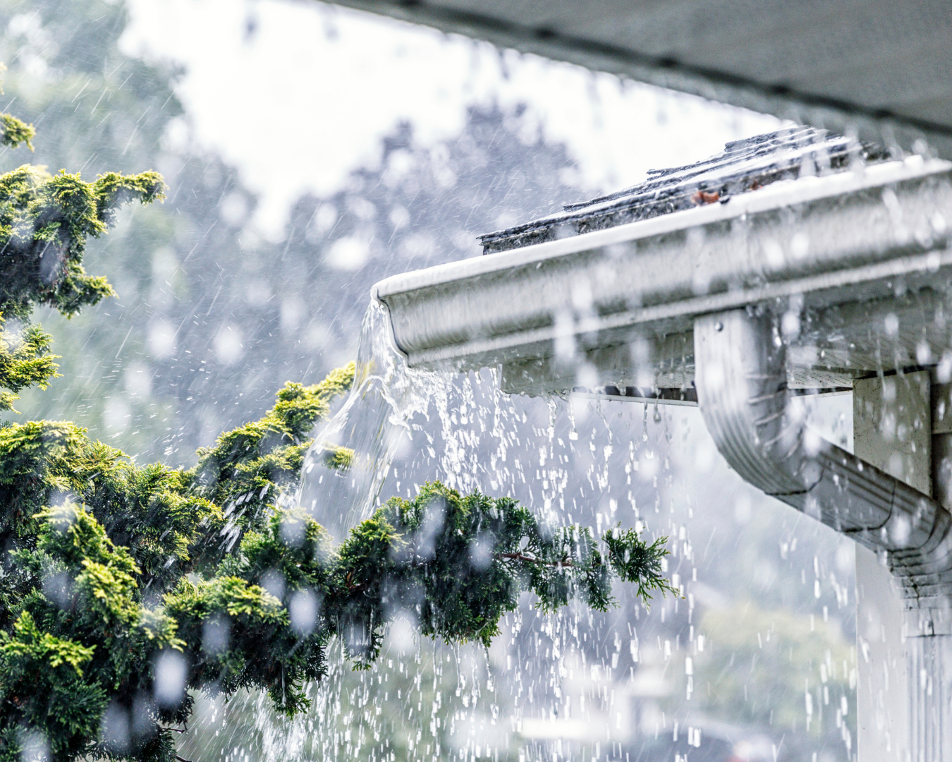 Rainwater overflowing from a home's gutter during a heavy rainstorm, illustrating how excess water can stain and damage a home's exterior if gutters aren't properly maintained.