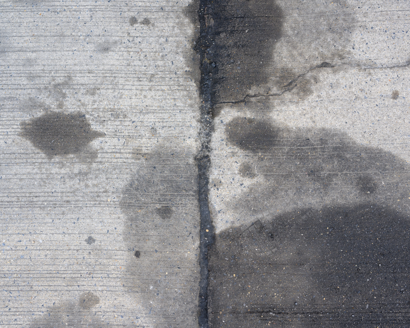 Close-up of concrete with dark black and gray staining, organic buildup, and discoloration across the surface.